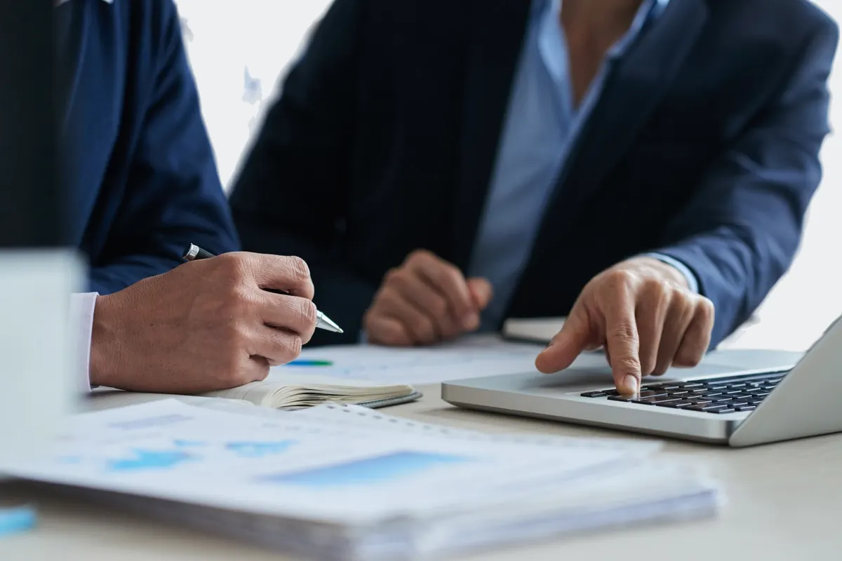 Two people in suits working with a laptop and printed business charts