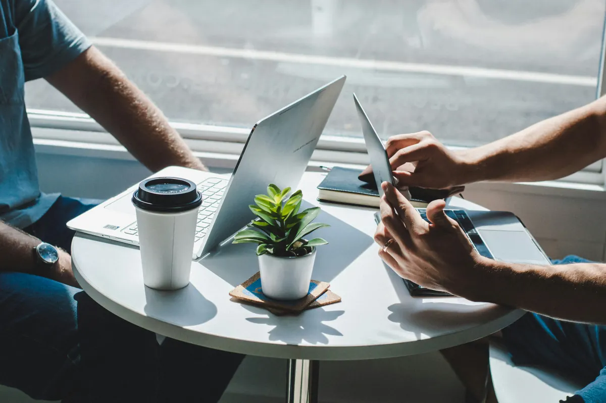Two people working on a laptop and a tablet at a small round table
