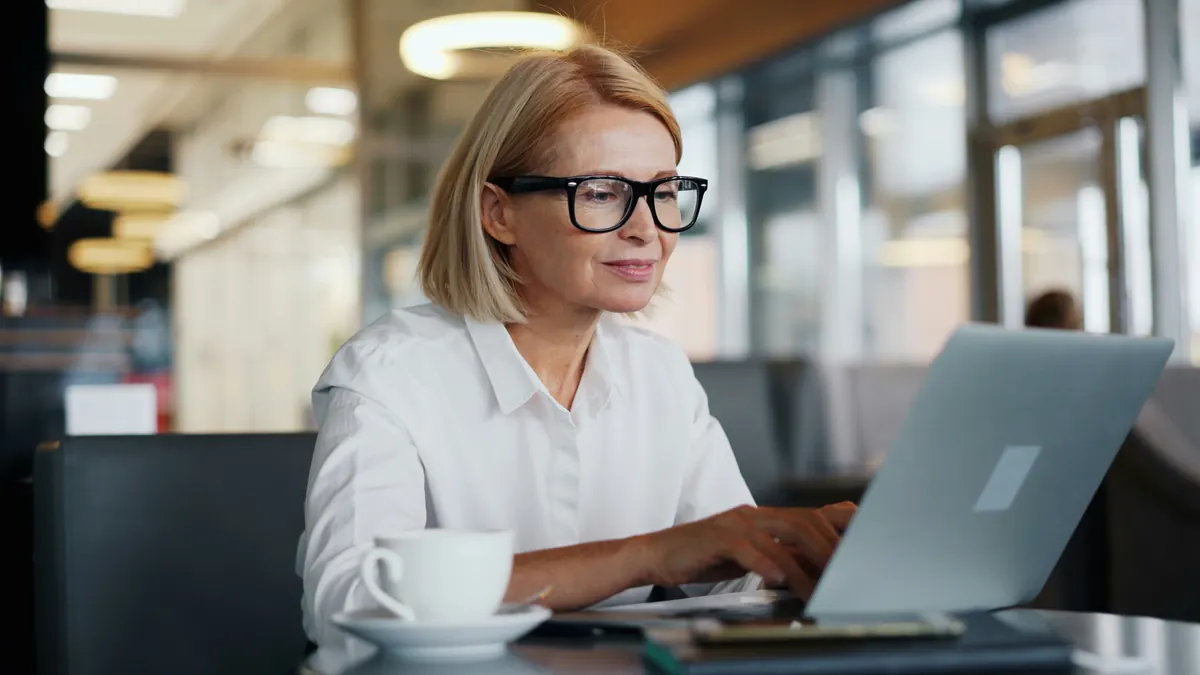 Woman with glasses smiling while she works on a laptop in an office